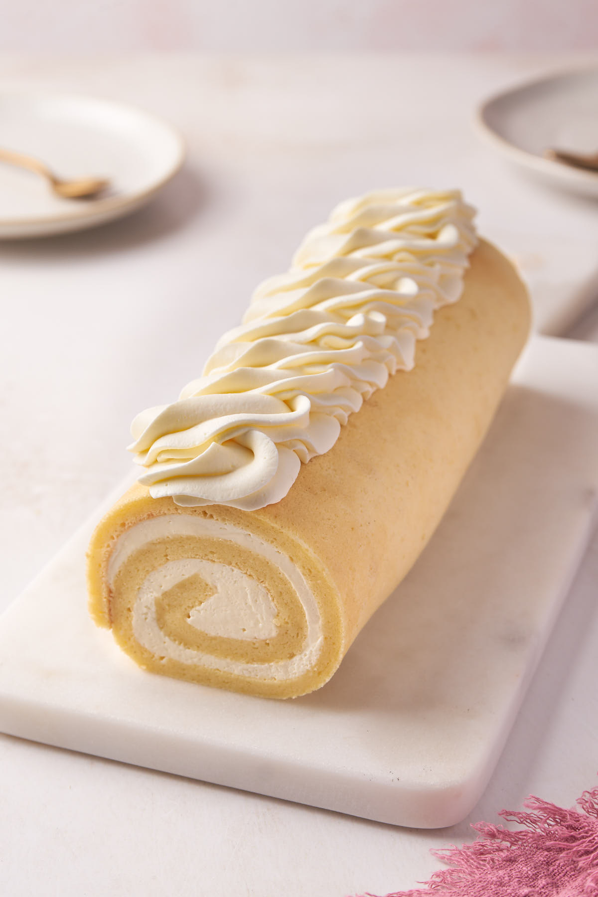 a vanilla roll cake with plates and spoons along.