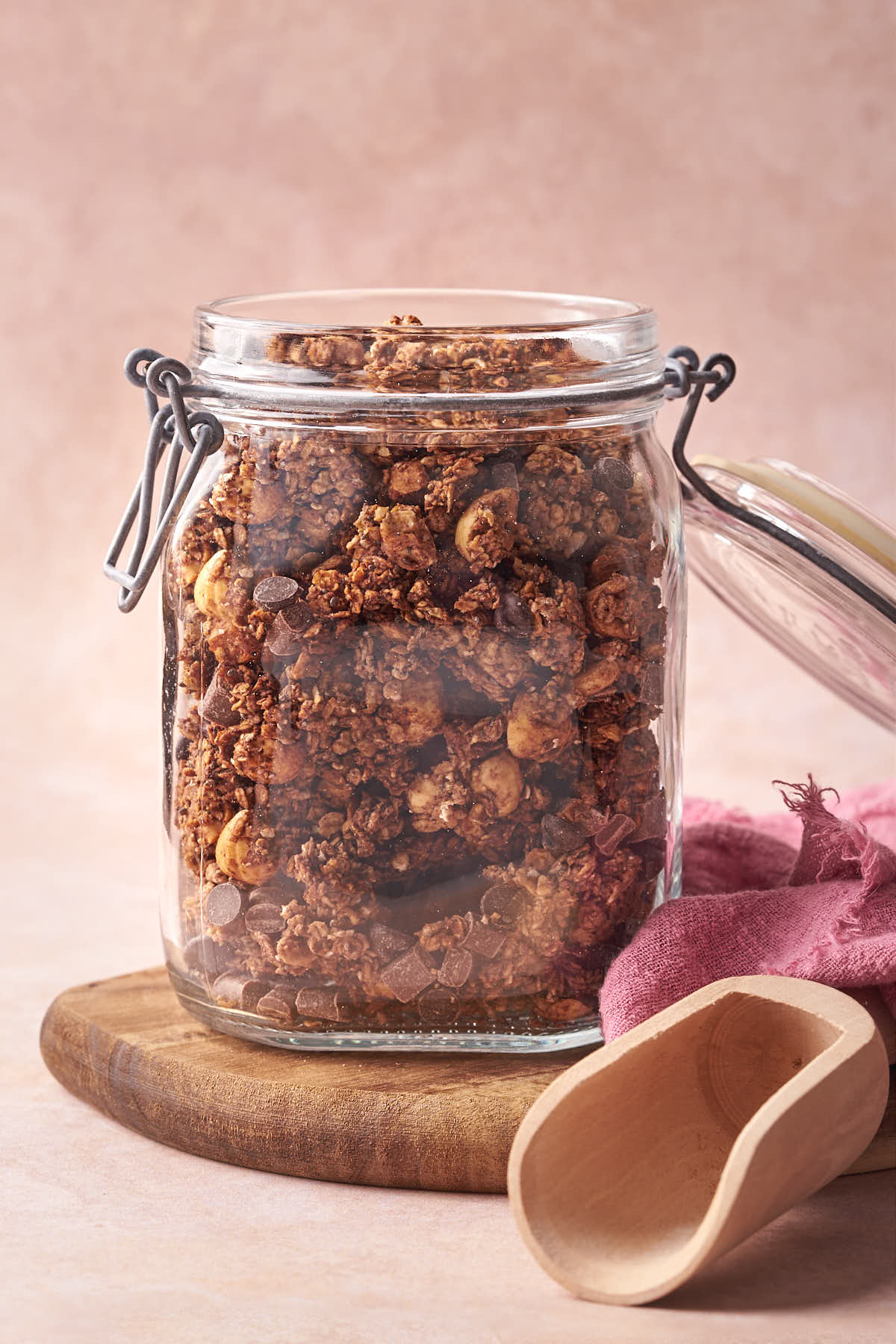 A glass jar filled with chocolate hazelnut granola, placed on a wooden board.