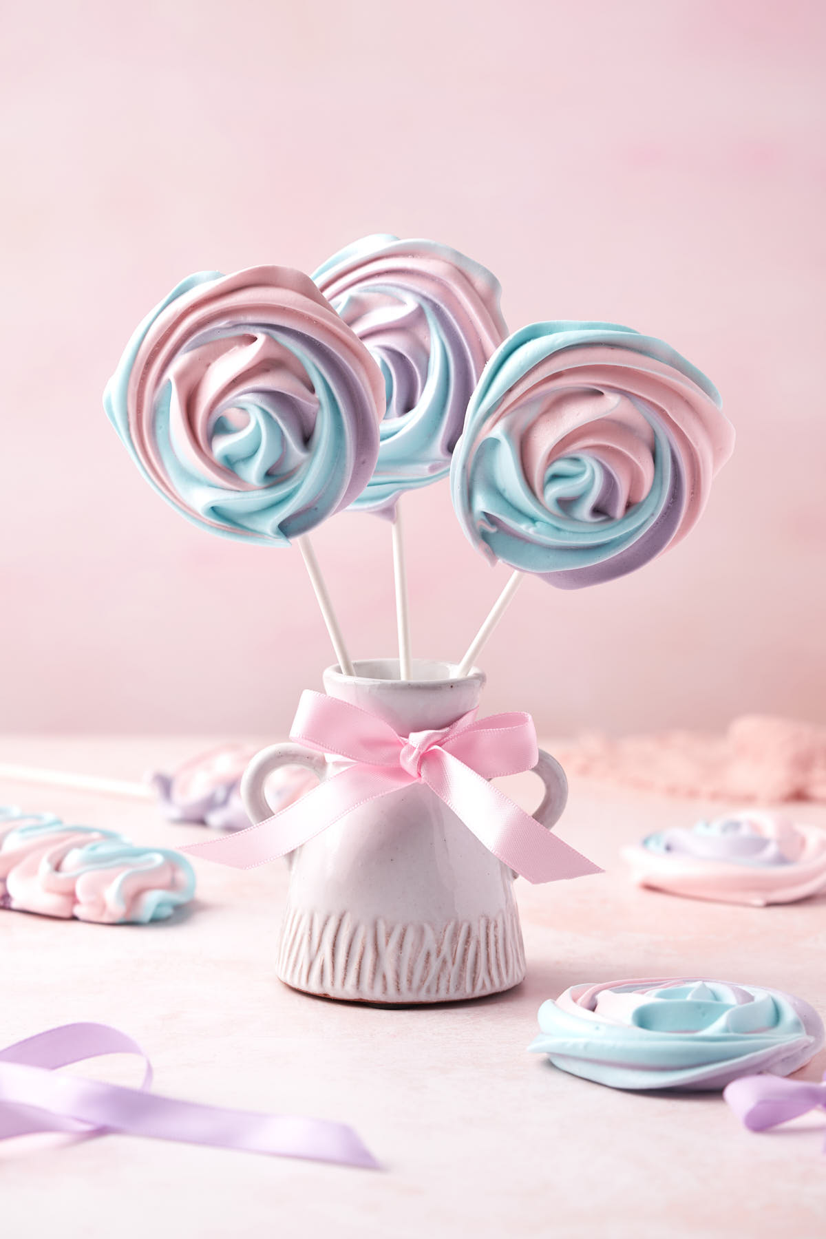 Three meringue pops in a ceramic jar, decorated with a ribbon.