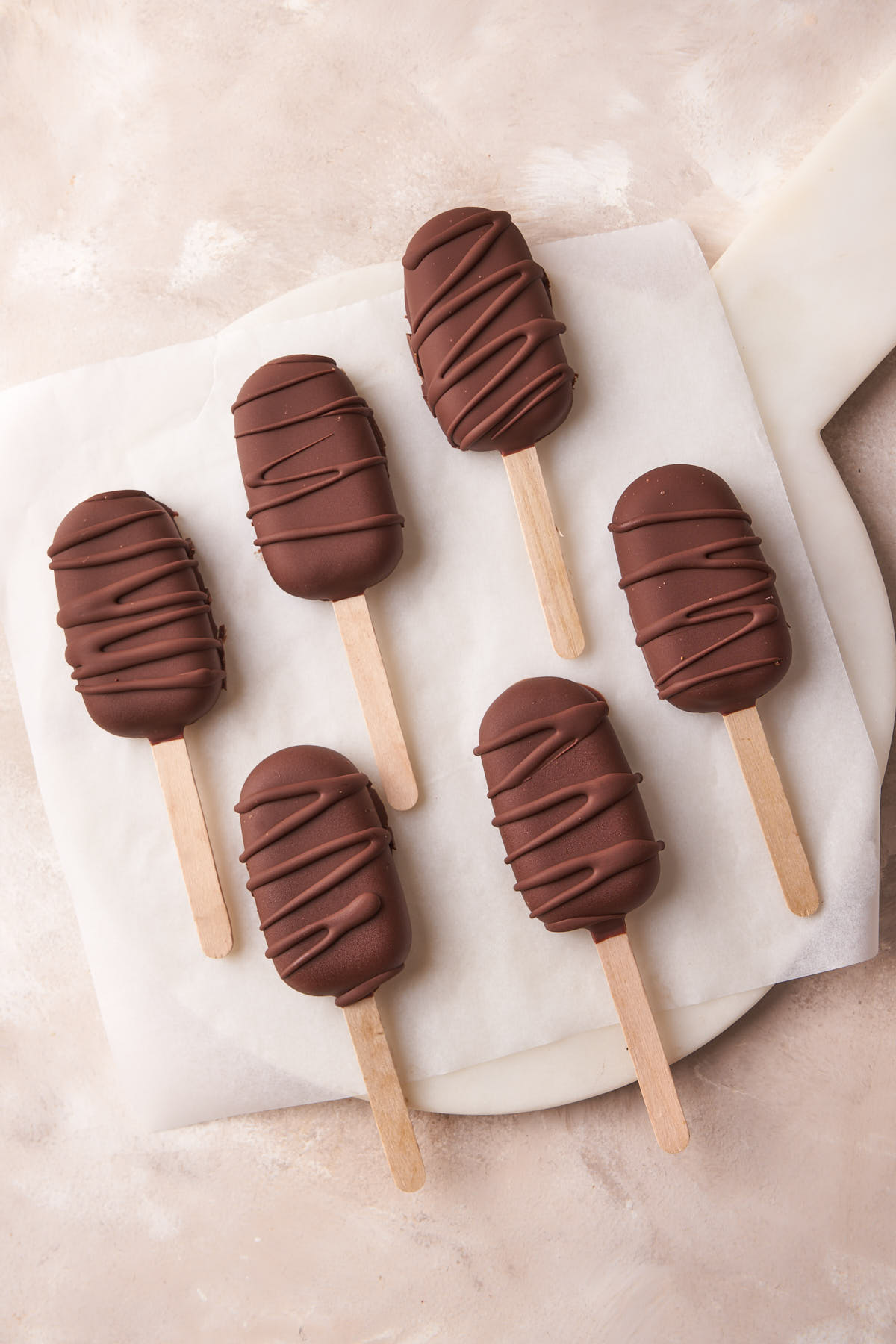 A batch of chocolate-covered ice cream bars arranged on a white marble board.