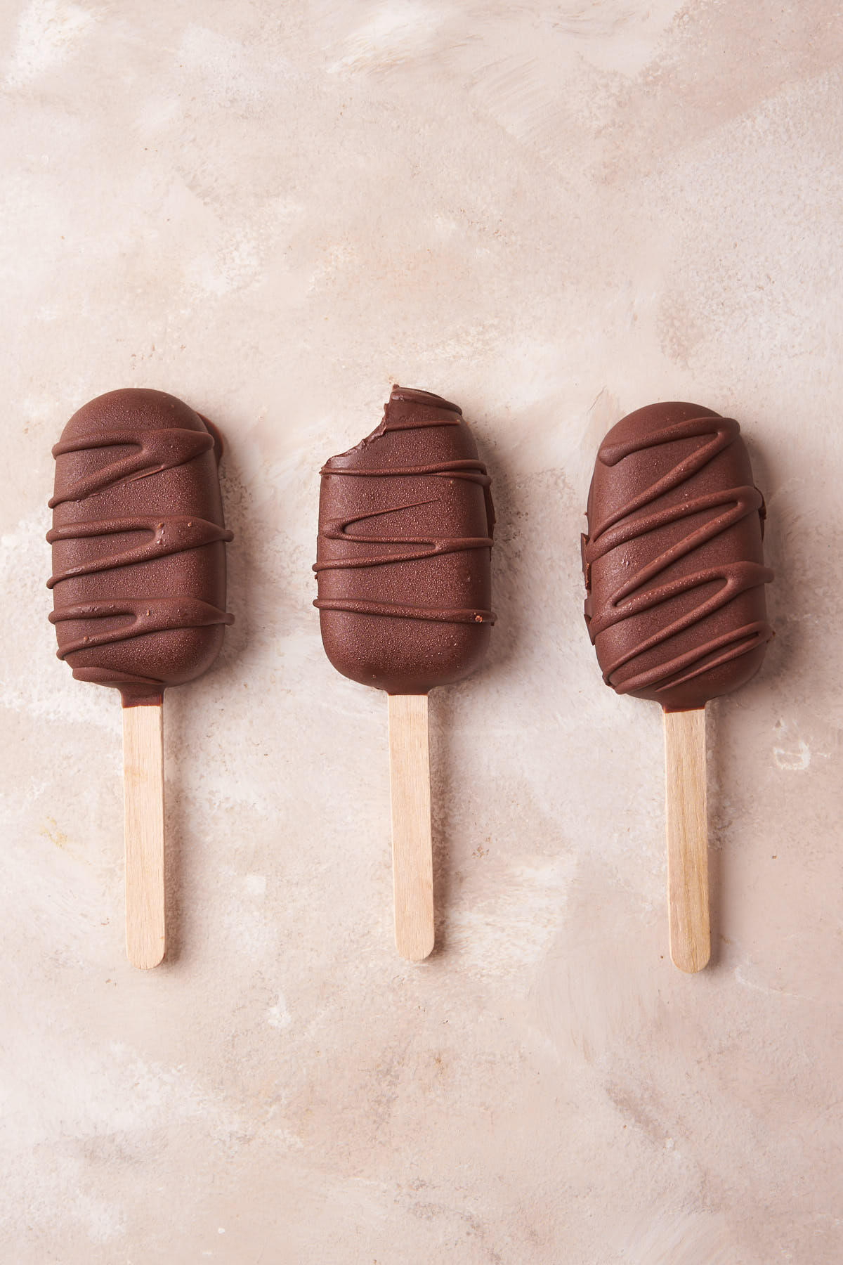 Three chocolate dipped ice cream bars, arranged side by side.