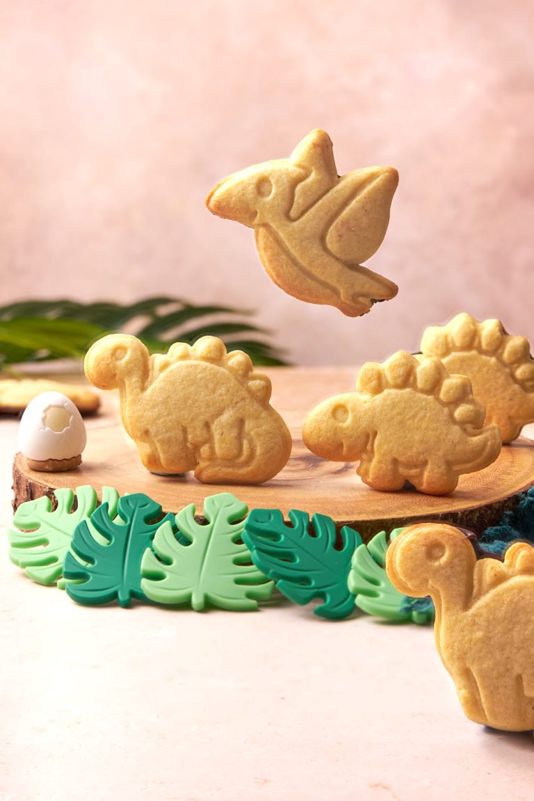 a couple of dinosaur cookies on a wooden board.